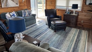 L’intérieur chaleureux d’un chalet, avec un revêtement mural en bois, un canapé, un fauteuil, une table basse et un tapis.