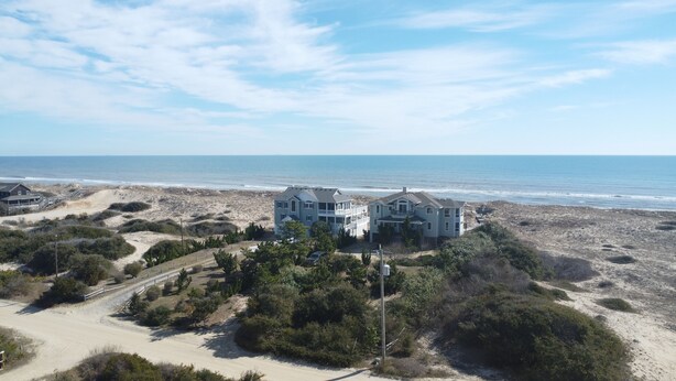 Une propriété située en bord de mer, avec une grande maison à plusieurs niveaux et un balcon offrant une vue sur l’océan.