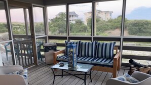 Un espace extérieur abrité, doté d’une terrasse en bois, d’une table en verre et d’un banc rembourré avec des coussins à rayures.