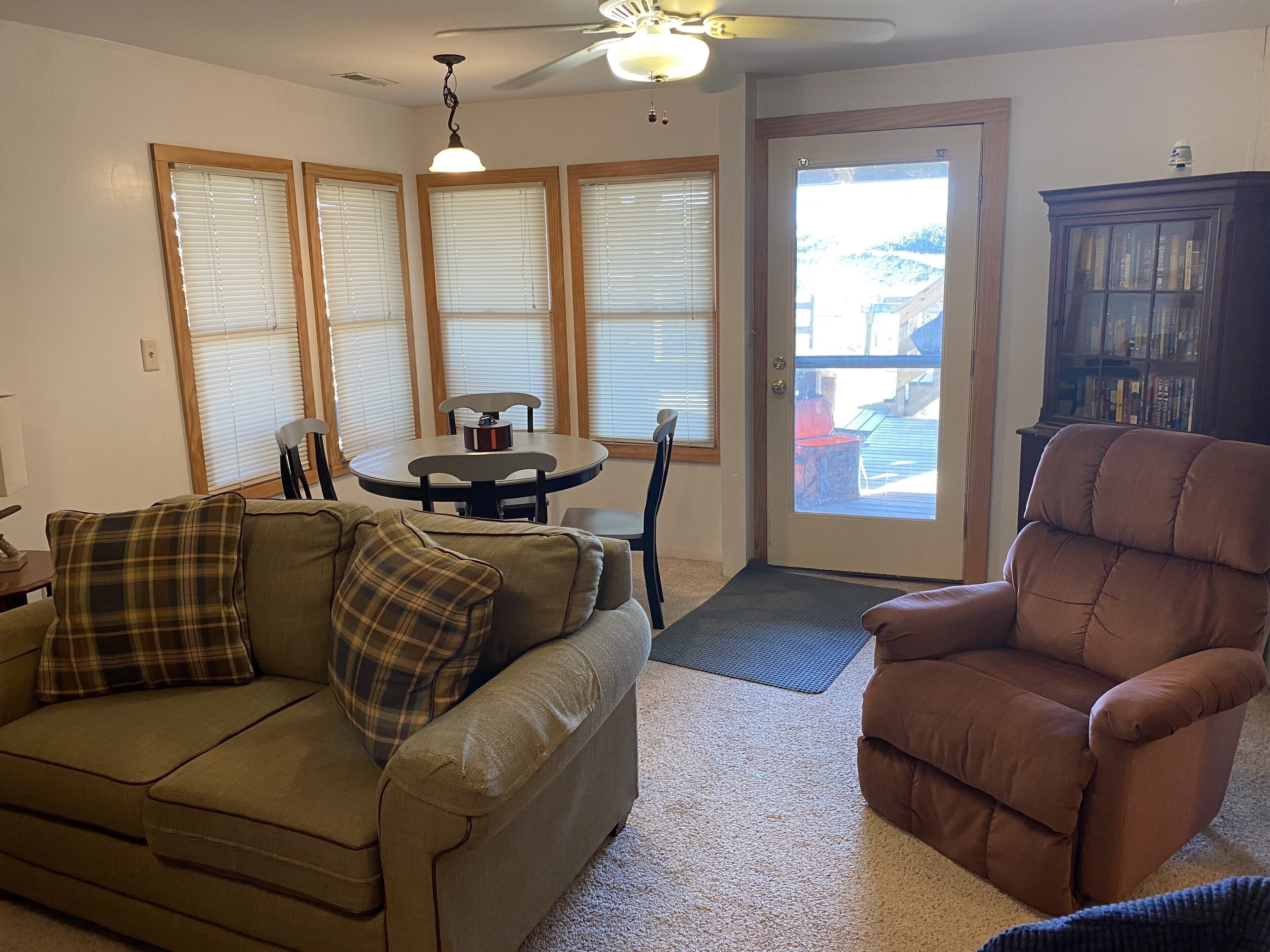 A living room with a sofa, armchair, dining table, and a bookshelf.