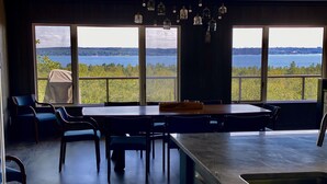 Moderni keittiö, jossa on suuri keittiösaareke, ruokailutila tuoleineen sekä suuret ikkunat, joista avautuu näkymä järvelle.