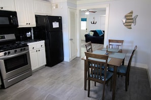 A kitchen with white cabinets, a black refrigerator, a stove, and a dining area with a table and chairs.