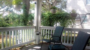A covered porch with white railings, two chairs, hanging planters, and a large tree in the background. - Galveston Getaway/Cruise, Fishing, Contractors & Beach (Galveston)