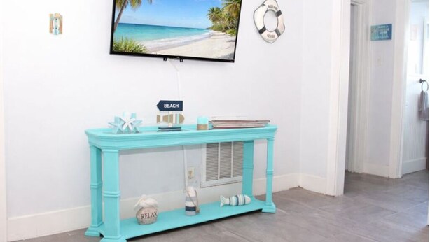 A turquoise console table with a 'BEACH' sign, a television displaying a beach scene, and a life preserver on the wall. - Galveston Getaway/Cruise, Fishing, Contractors & Beach (Galveston)