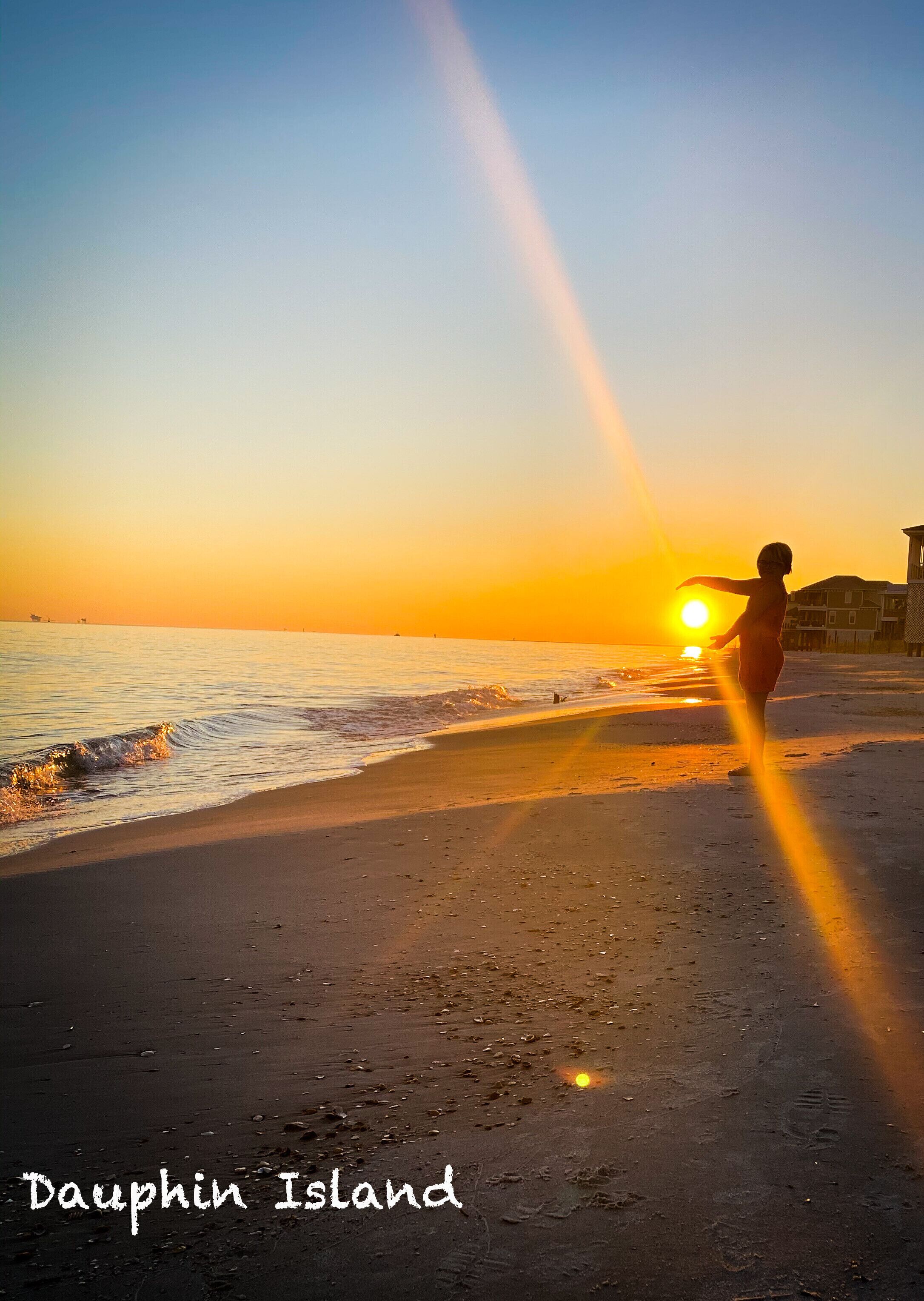 Une scène de plage au coucher du soleil, avec une personne debout, face au soleil, et le texte « Dauphin Island » en bas.