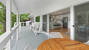 A covered outdoor deck with white chairs and a wooden table, leading to a modern kitchen with a refrigerator and island. - Luxury A-Frame on Lake LBJ, Wakesurf Paradise, Two-Story Dock, Sleeps 16 (Kingsland)