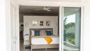 Une chambre à coucher comprenant un lit, des tables de chevet, un ventilateur de plafond et une vue sur l’extérieur grâce à une porte-fenêtre coulissante.