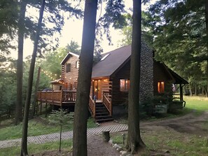 A log cabin with a wooden deck and a stone wall, surrounded by trees.