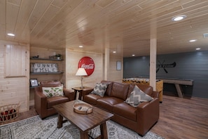 A cozy room with a brown leather sofa, a wooden coffee table, and a foosball table. There is a Coca-Cola sign on the wall and a 'Tunnel 1/8 Mile' sign. - Little Fork Lodge - Three Lakes Lakefront on the trails with Firepit/Game Room (Three Lakes)