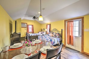 A room with a dining table set for four, a bed with floral bedding, a ceiling fan, and a door with curtains. - Double Retreat · Poconos Nature Escape (Pleasant Mount)