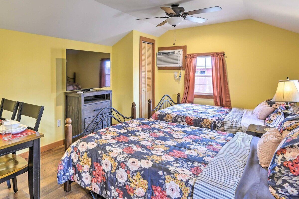 A bedroom with two beds, a ceiling fan, a desk with a chair, and a window with curtains.
