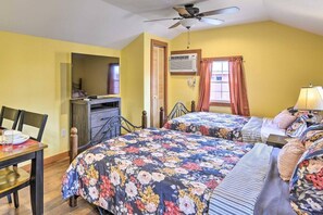 A bedroom with two beds, a ceiling fan, a desk with a chair, and a window with curtains.