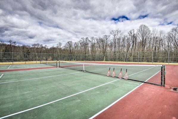 An outdoor tennis court with a net, surrounded by a fence and trees.