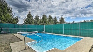 A rectangular swimming pool with a metal ladder and a green fence surrounding it.