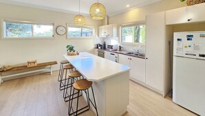 A modern kitchen with a central island, bar stools, pendant lighting, and a refrigerator with magnets. - Summer House - Cosy, comfortable, located close to town (Robe)