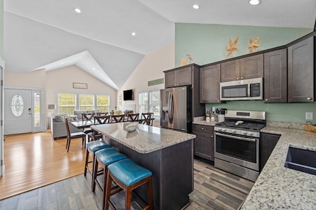 A spacious kitchen with dark cabinets, a large island, and a dining area with blue bar stools.