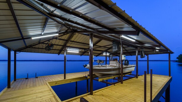 Un muelle de madera con un área techada, un bote y agua tranquila.