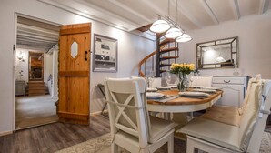 A dining area with a wooden table, white chairs, and a chandelier. A staircase is visible in the background. - Suncroft - sleeps 8 guests  in 3 bedrooms (Banbury)