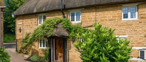 A stone building with a thatched roof, a wooden door, and a small garden area.