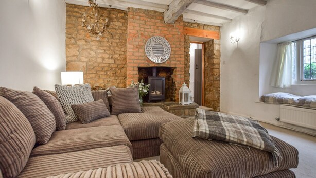 A cozy living room with a brick fireplace, a large sectional sofa, and a window with curtains. - Suncroft - sleeps 8 guests  in 3 bedrooms (Banbury)