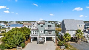 A multi-story residential building with a balcony on the second floor, a front porch, and a driveway leading to a gated entrance. - Second Row, 4 Bedroom/3 Bath Home w/ Private Pool and Dock. Sleeps 10 (Holden Beach)