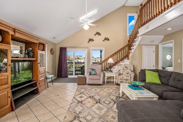 Relax in this spacious living room with a high ceiling and ceiling fan, featuring a large window with a view of the surrounding area.