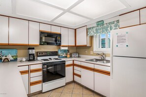 Enjoy a meal with a view of the beach from this kitchen, featuring a microwave, stove, oven, and refrigerator.