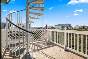 Staircase leads to an upper level from a spacious deck with a white railing.