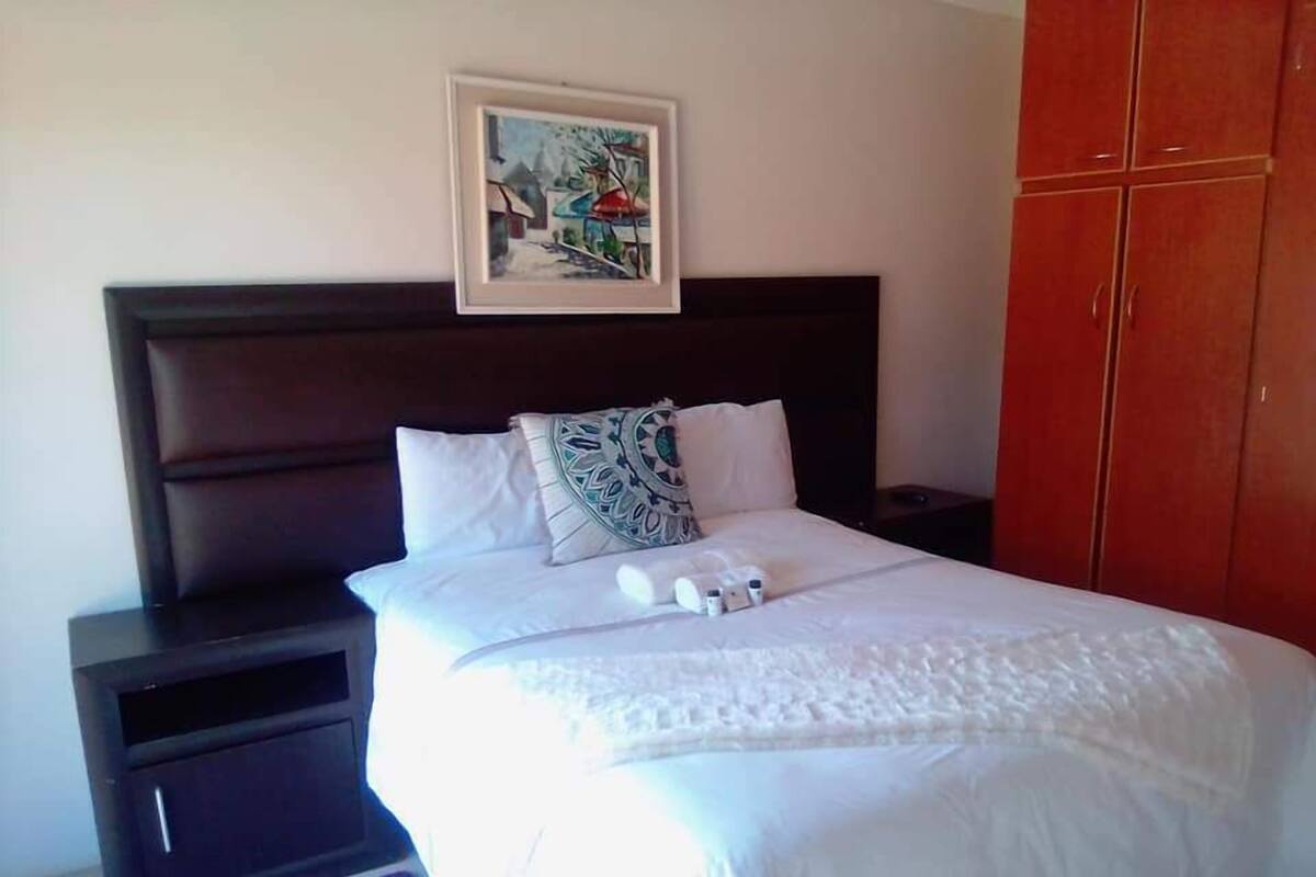 A neatly made bed with white linens and a decorative pillow, a framed picture on the wall, and a wardrobe to the right.