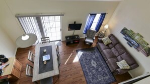 A living room with a sofa, a TV, a dining table with chairs, and a large window with blinds. - WaterWay - Balcony view of Lake Taneycomo (Branson)