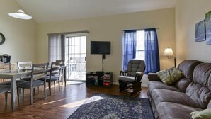 A living room with a sofa, a television, a dining table with chairs, and a window with curtains. - WaterWay - Balcony view of Lake Taneycomo (Branson)