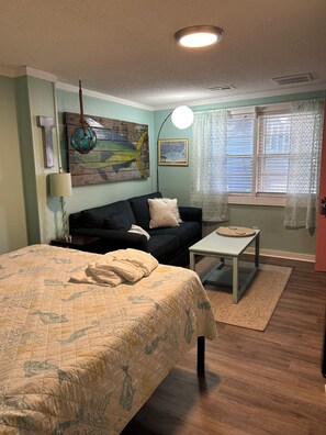 Une pièce confortable avec un lit, un canapé, une petite table et une fenêtre avec des stores.