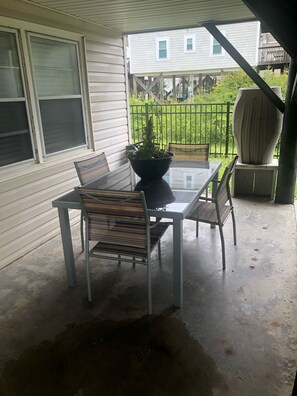 Une terrasse couverte avec une table et des chaises, un pot de fleurs et une vue sur un quartier résidentiel, avec une clôture et des maisons.
