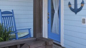 En veranda med en blå stol, en träbänk och en blå dörr med en gardin.