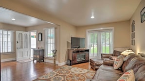 A spacious living room with hardwood flooring, a leather sofa, a fireplace, and a television.