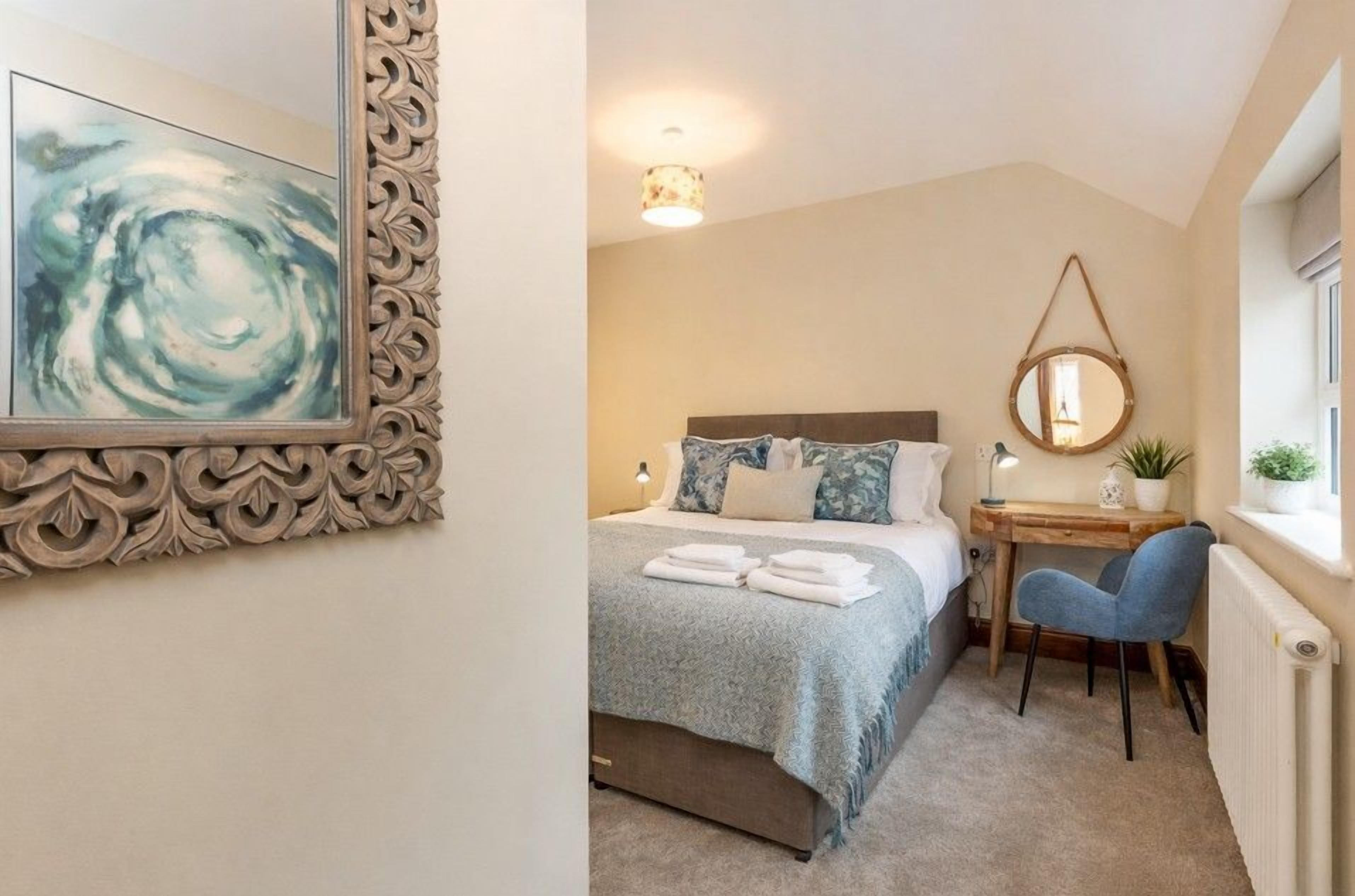 A bedroom with a bed, bedside table, chair, and a wall-mounted mirror.