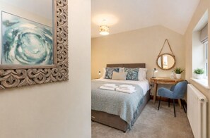 A bedroom with a bed, bedside table, chair, and a wall-mounted mirror. - The Creamery Cottage (York)