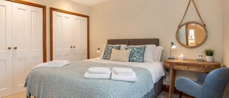 A bedroom with a bed, bedside table, chair, and a mirror on the wall.