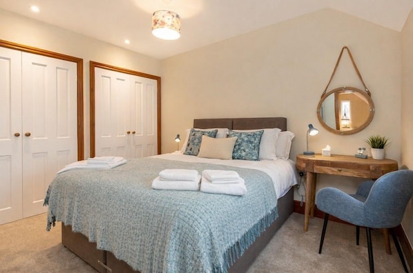 Un dormitorio con cama, mesita de noche, silla y espejo en la pared.