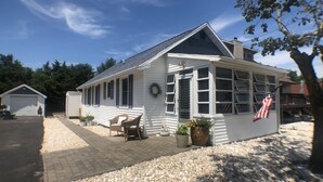 A white house with a large window and a door, a porch with two chairs, and an American flag. - Perfect beach cottage for your Lewes vacation! 10 Texas (Lewes)