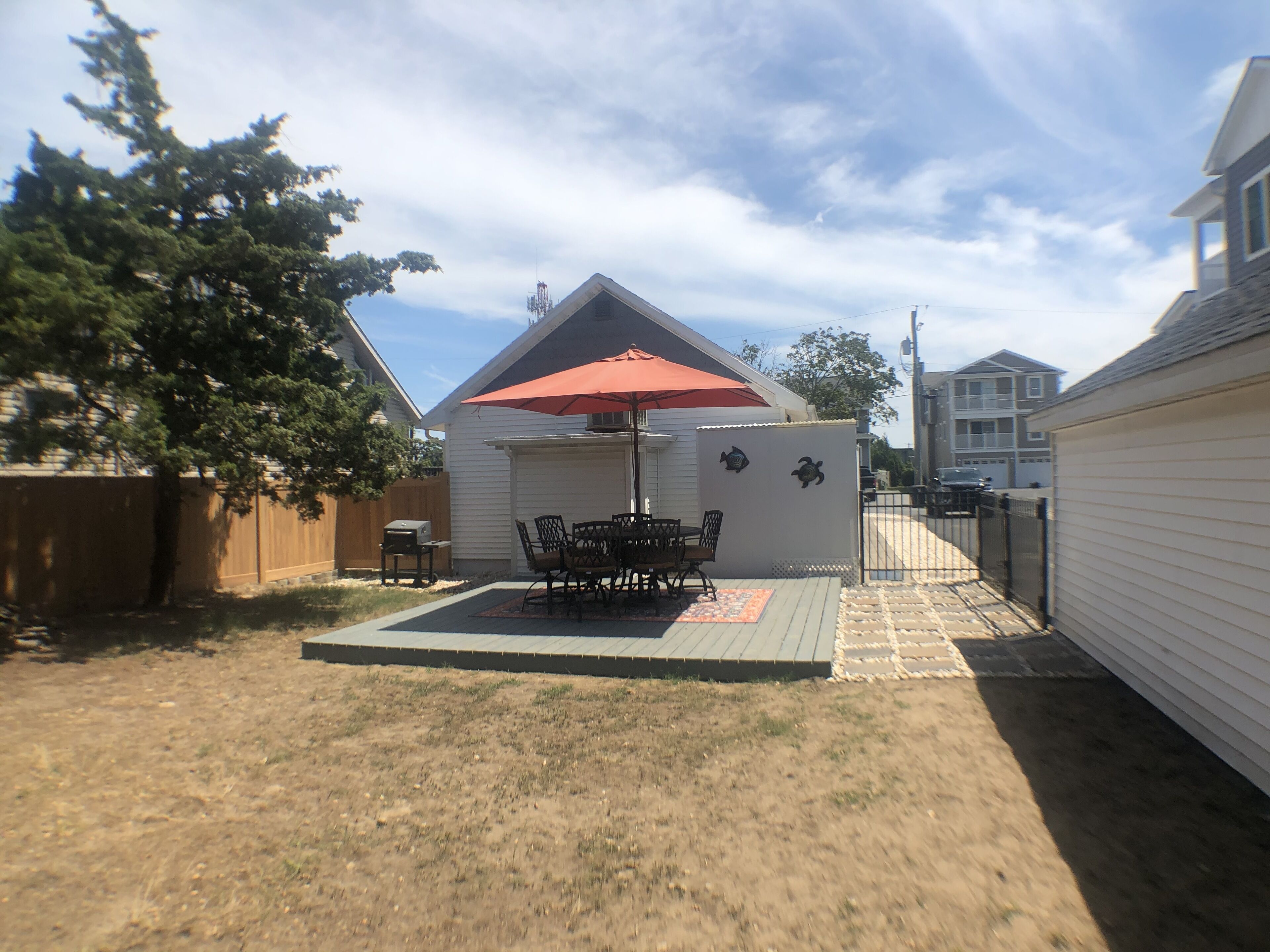 Um quintal com mesa e cadeiras no alpendre, churrasqueira e área coberta com guarda-sol.