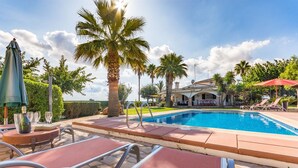 A swimming pool with lounge chairs, palm trees, and a building in the background. - Charming Villa “Finca Santa Eulalia Petit” with Porch and Pool (Can Picafort)
