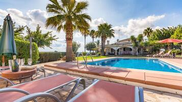 A swimming pool with lounge chairs, palm trees, and a building in the background.