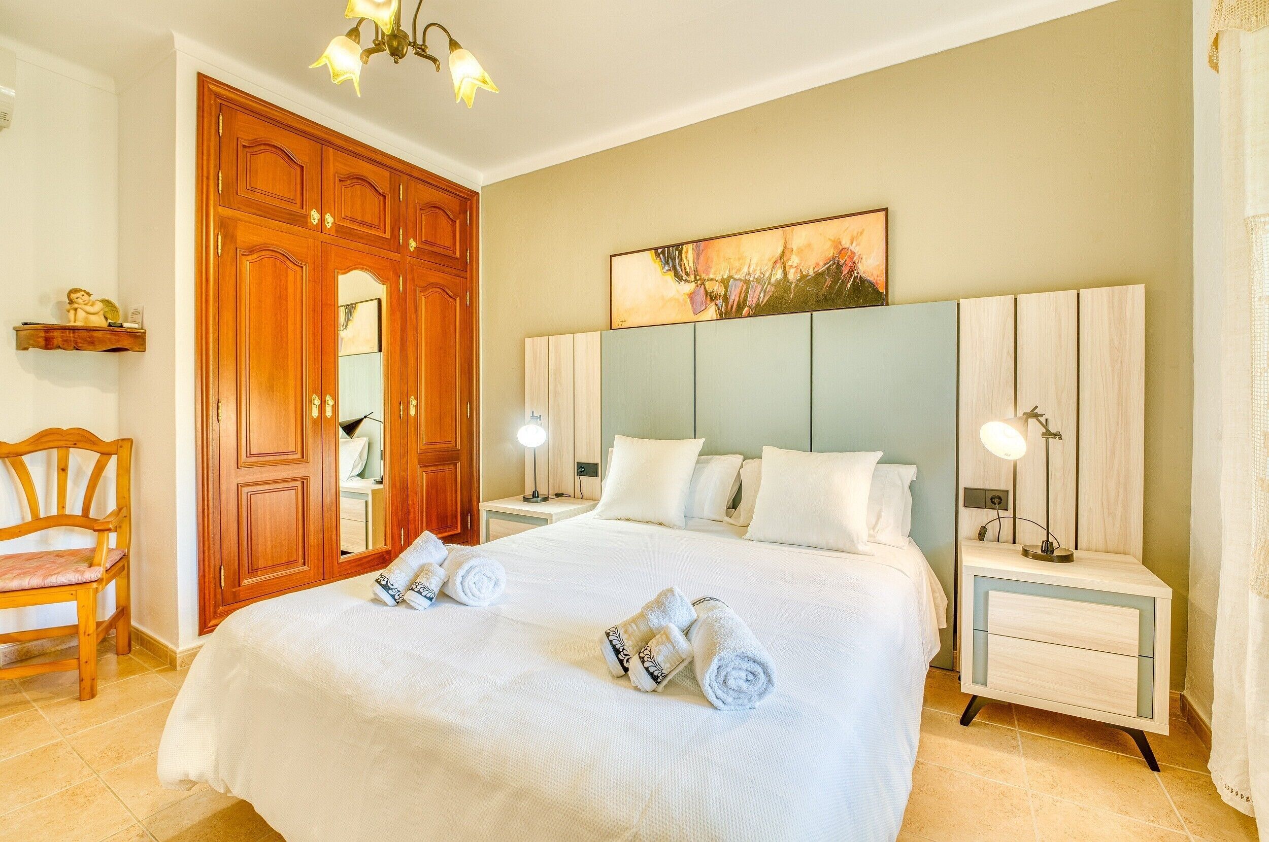 A hotel room with a large bed, wooden wardrobe, bedside tables with lamps, and a painting on the wall.