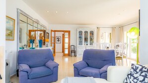A living room with a sofa, a coffee table, and a dining area with chairs and a table. - Villa 'La Vinya del Beato 1950' with Mountain Views, Private Pool, and Garden (Port de Pollença)
