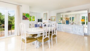 A spacious dining area with a white table and chairs, a large mirror, and a view of the outdoors. - Villa 'La Vinya del Beato 1950' with Mountain Views, Private Pool, and Garden (Port de Pollença)