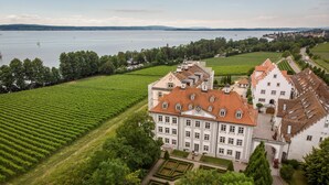 A large, historic building with a symmetrical facade, surrounded by lush green vineyards and a body of water in the background. - Schloss Kirchberg – Apartment Rosé (Immenstaad)