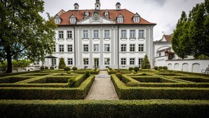 A large, symmetrical building with a central entrance, surrounded by a formal garden with geometric hedges. - Schloss Kirchberg – Apartment Rosé (Immenstaad)