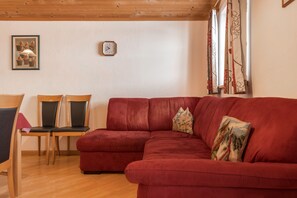 A red sofa with a cushion, wooden chairs, a clock, and a framed picture on the wall.