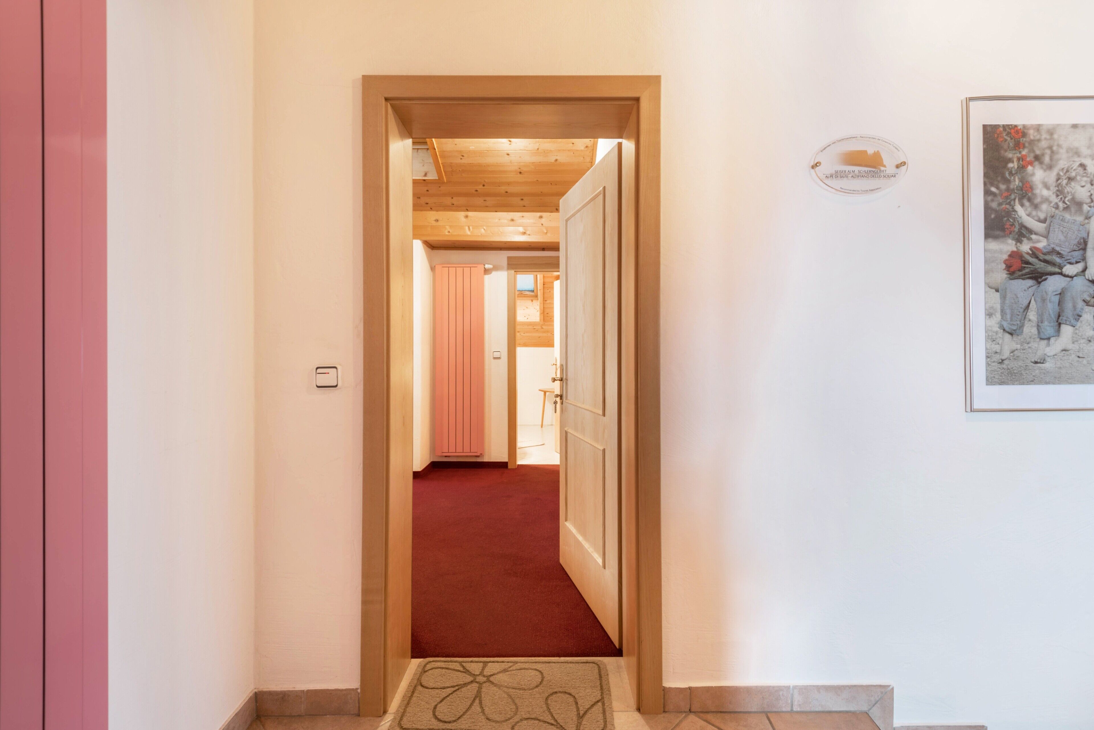 A hallway with a red carpet leading to a room with a wooden ceiling and a door.